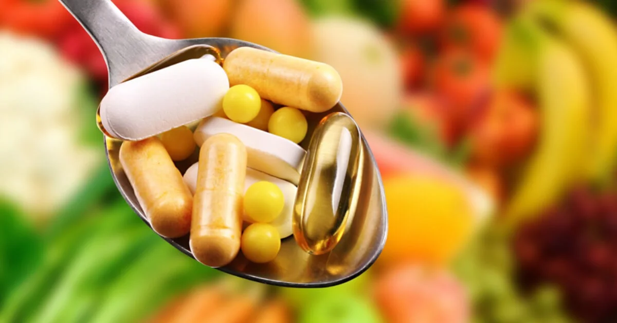 a spoon of supplements with fruit and veg in the background