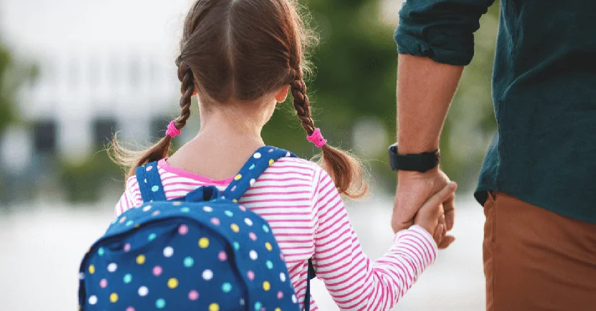 A dad holding his daughters hand on the way to school